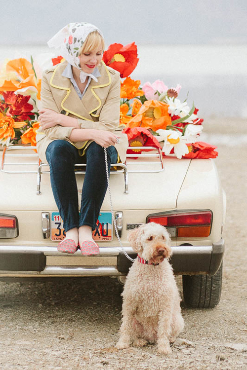 Brittany sits on the back of a convertible filled with paper flowers holding a dog's leash.