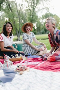 Three women wearing red, white, and blue laugh at a fourth of july picnic