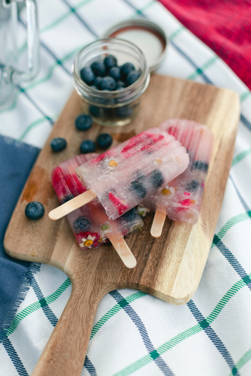 red, white, blue popsicles to celebrate 4th of july on a wood cutting board on a green and white windowpane picnic blanket