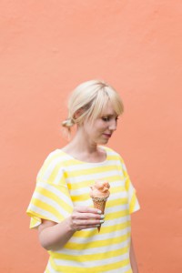 Brittany wearing a striped yellow dress in front of a pale orange wall eating canteloupe sorbet