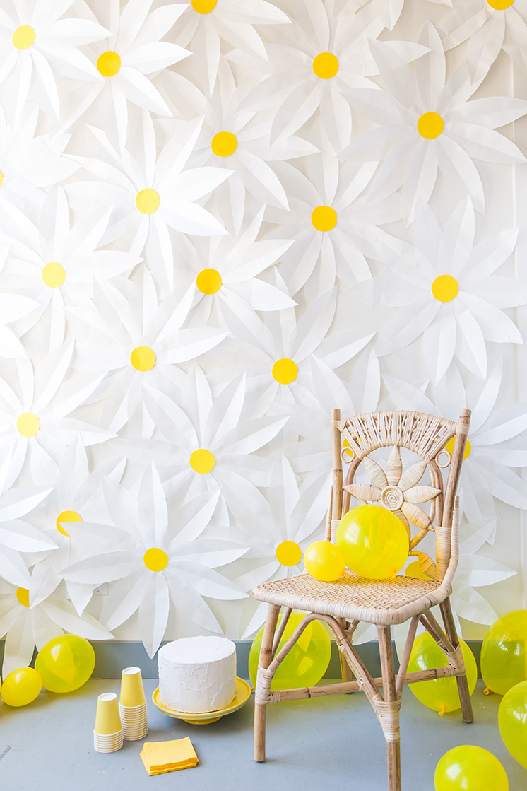 Brittany stands in front of a paper daisy-covered wall wearing a yellow dress.