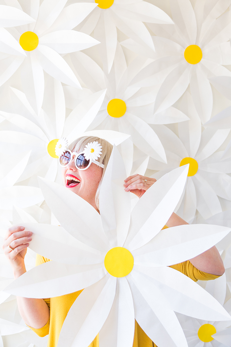 Brittany stands in front of a paper daisy-covered wall wearing a yellow dress.