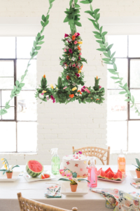 A floral upcycled chandelier with paper greenery hangs over a party table.