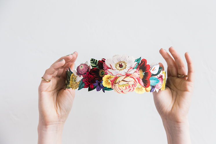 A printable flower crown in purple, yellow, pink, white red, and blue being held up by two hands. 
