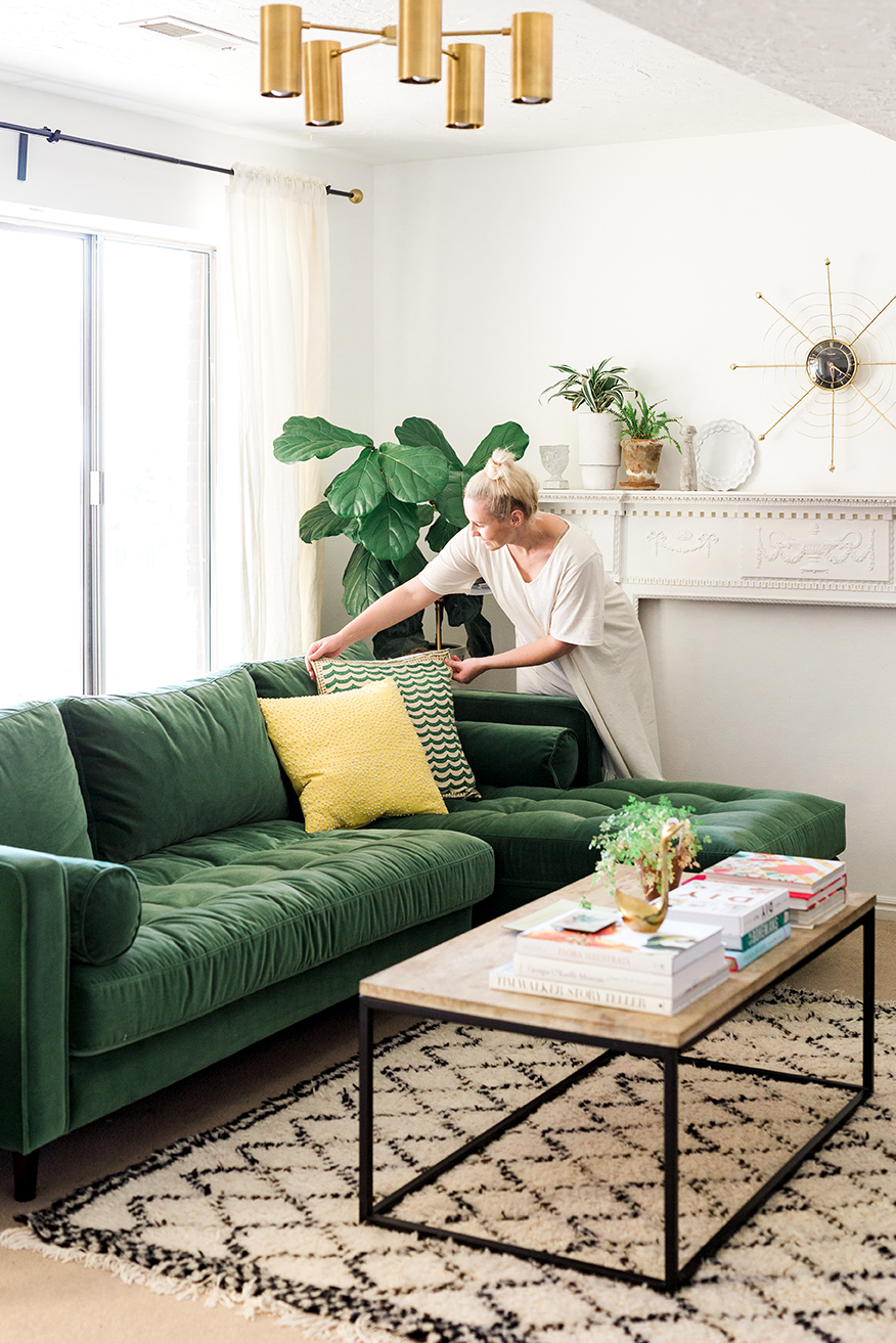 Brittany adjusts pillows on a beautiful green sofa in a light-filled room