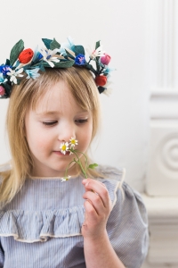 A little girl wears a paper flower crown and smells some little flowers.