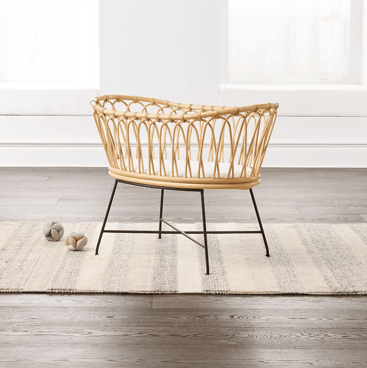 A rattan bassinet with metal legs in a light-filled nursery