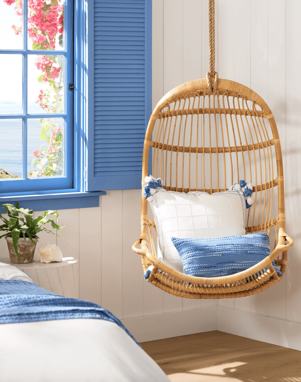 Rattan hanging swing in a light-filled room with blue pillows and accents