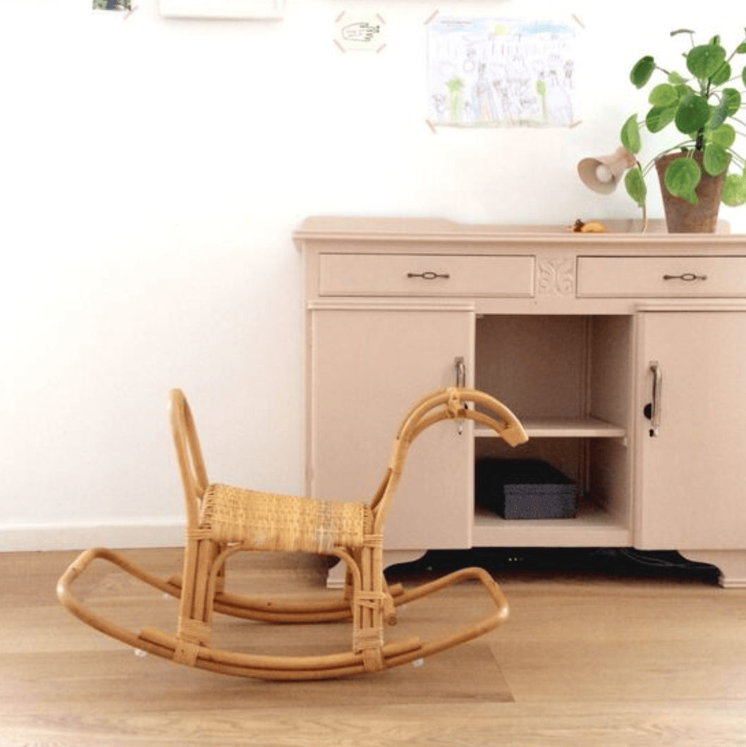 Rattan rocking horse in front of a cabinet.
