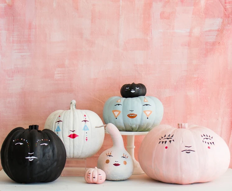 painted pastel pumpkin faces against a pink background