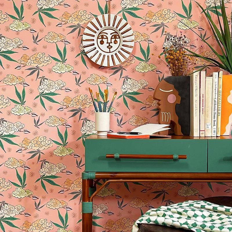 Blush wallpaper with botanical accents by Justina Blakeney. The space is decorated with a green desk, books, and a sun-shaped wall decoration.