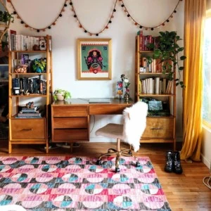 A colorful bohemian room with a pink, cyan, and blue rug, yellow curtains, and warm wooden furniture.