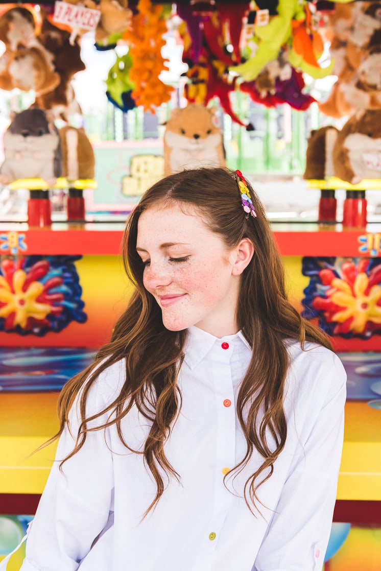 a white woman with brown hair wears a white blouse with rainbow buttons