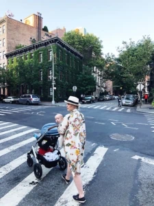 Brittany wearing a floral dress and pushing a stroller across a street in New York City