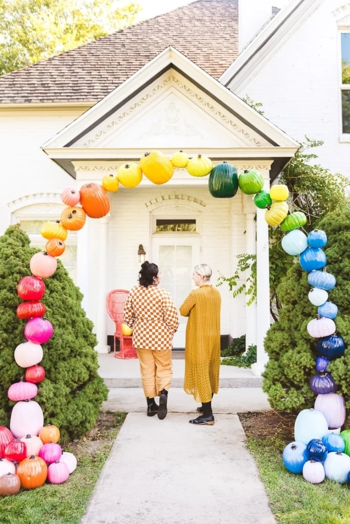 Brittany and Sammy wearing yellow and walking under a rainbow pumpkin arch