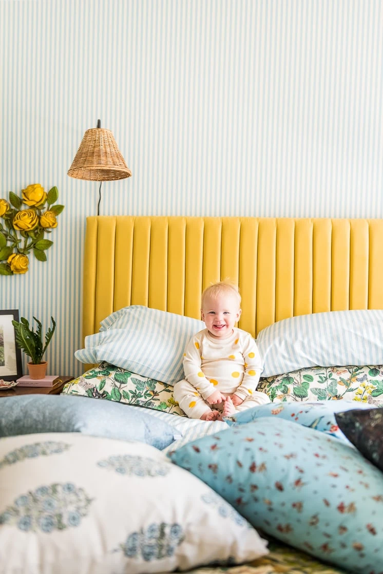 Baby Jasper sits on a blue-themed bed with a yellow headboard. Blue and white striped wallpaper is behind him.
