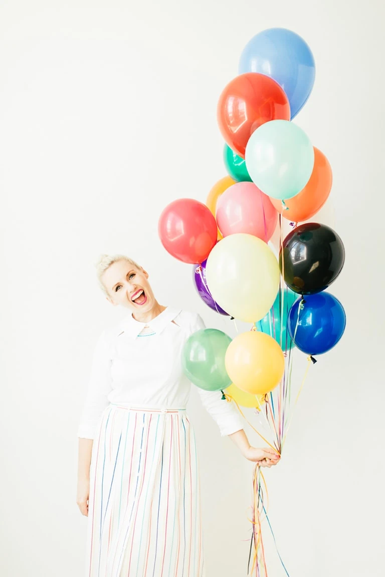 Brittany wearing a white dress and holding a bundle of rainbow balloons