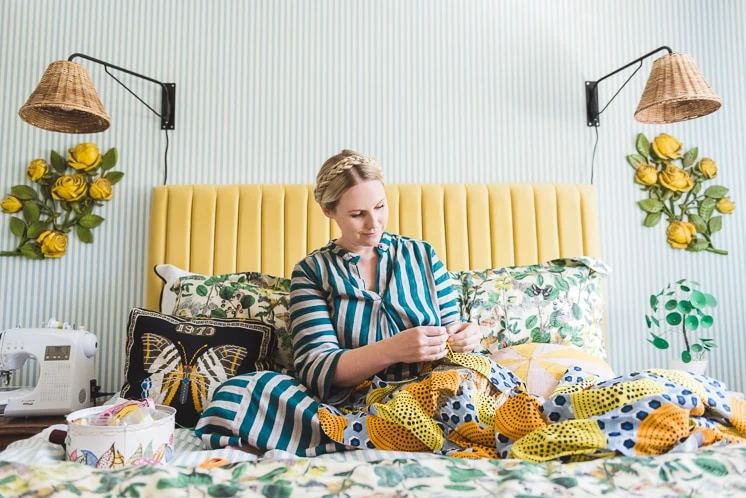 Brittany Jepsen on her bed sewing a dress in a colorful room