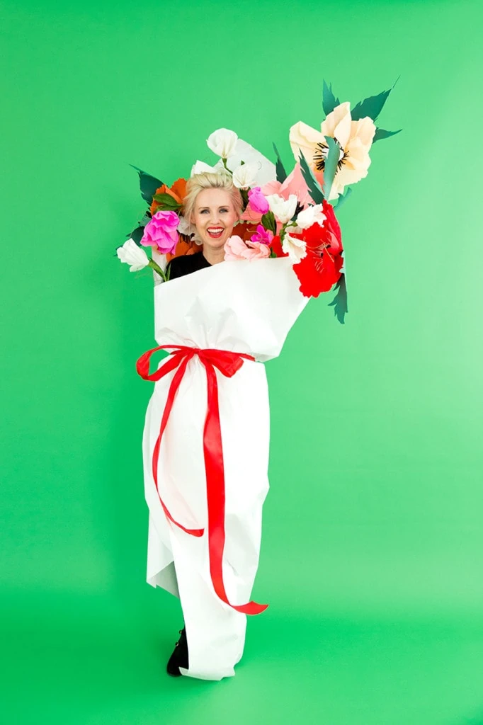 Brittany wearing a bouquet costume with paper flowers and a white paper wrapper against a green backdrop