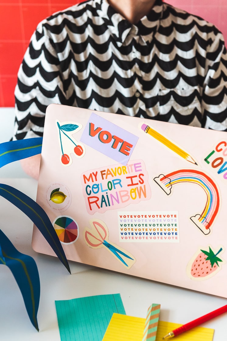 A woman sits behind a laptop, which is covered in rainbow, fruit themed, and office supply stickers.