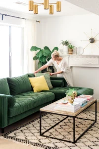 Brittany arranges pillows on a green velvet sofa in a light-filled room