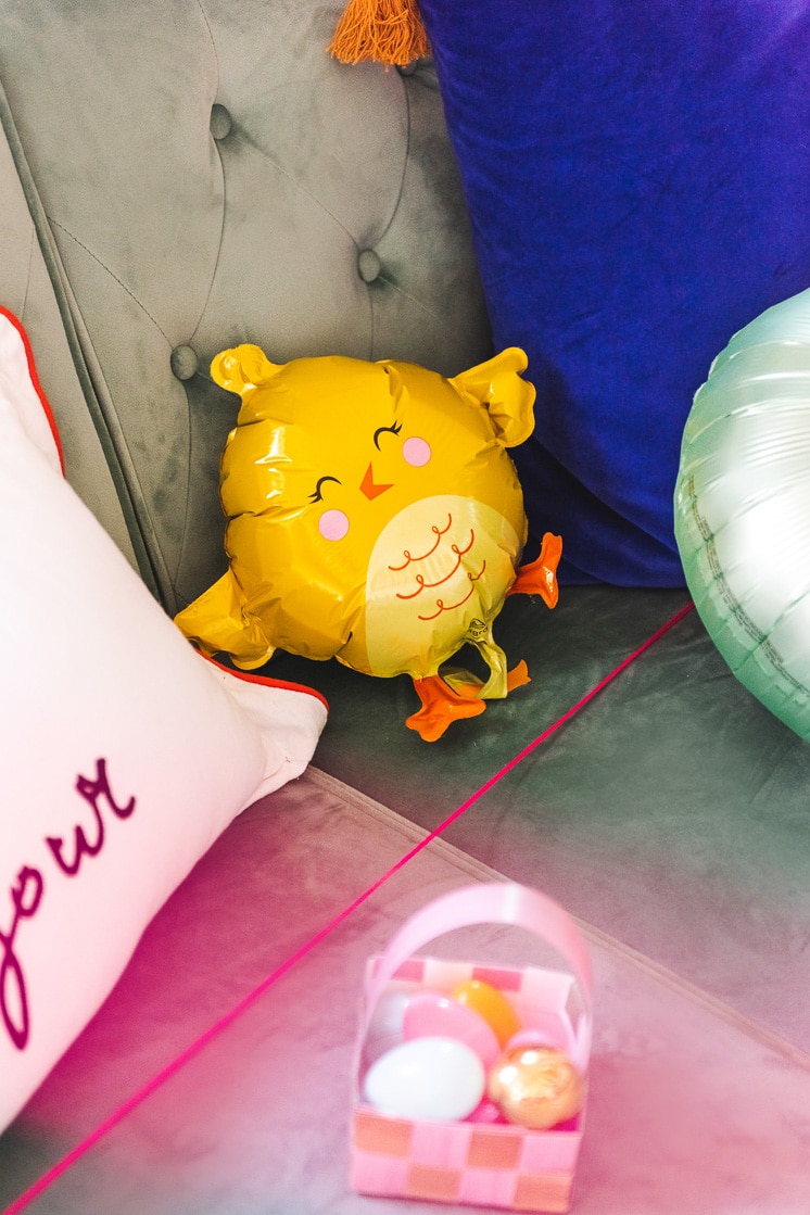 A little yellow chick balloon on a couch with colorful pillows and an Easter basket. 