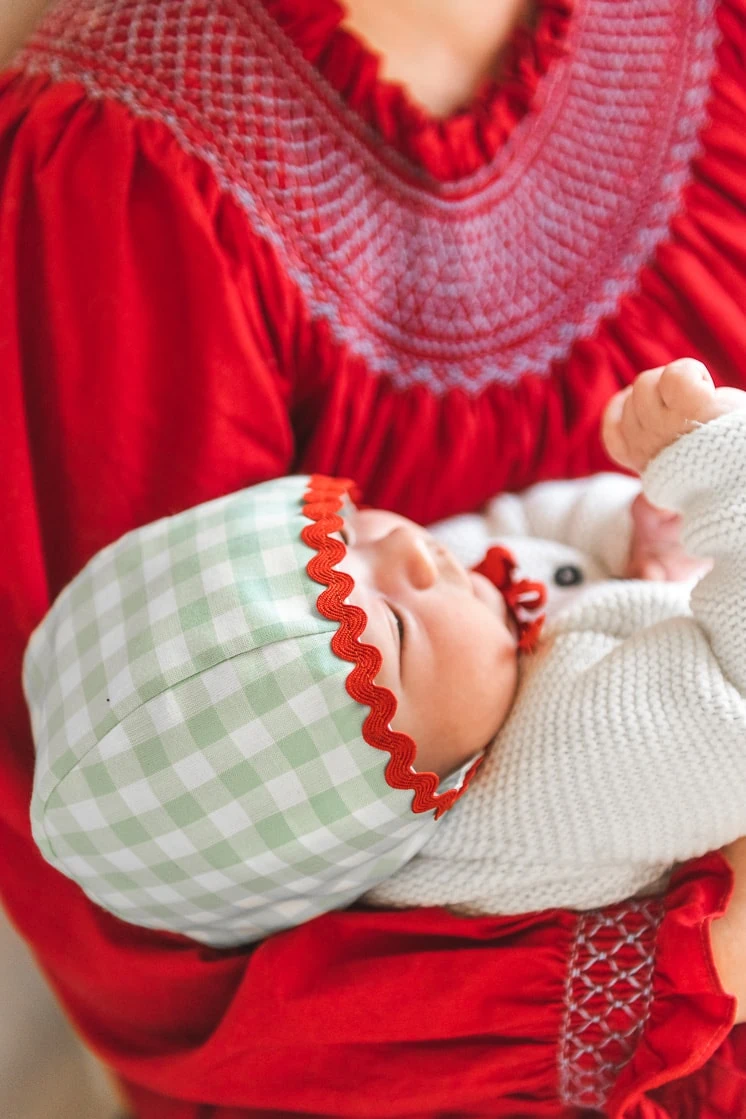 baby in green and red bonnet held by woman in a red dress