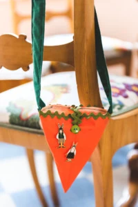 A carrot bag hangs on the back of a chair with two easter bunny pins attached to it.
