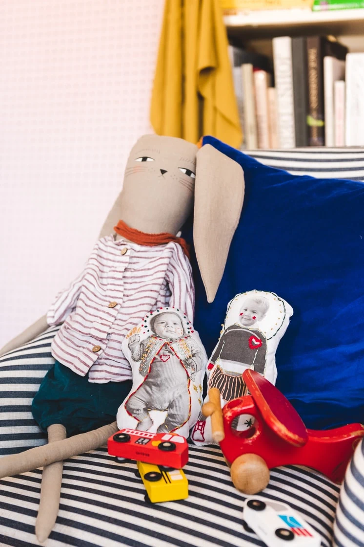 Two embroidered plush dolls on a couch with a plush rabbit and colorful toys.