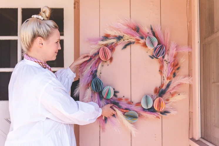 Brittany hangs a pastel floral Easter wreath on a pink exterior wall