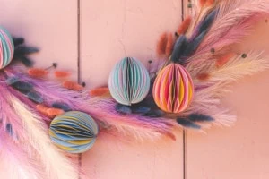 Paper honeycomb Easter Eggs on a pastel floral Easter wreath on a pink wall.
