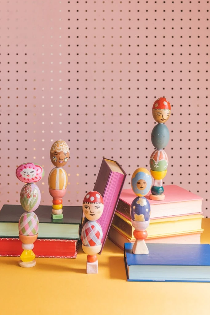painted Easter egg columns perched on colorful books against a yellow and pink background.