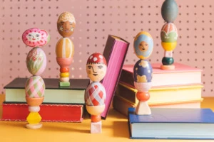 Colorful painted easter egg columns stacked on books against a pink background.