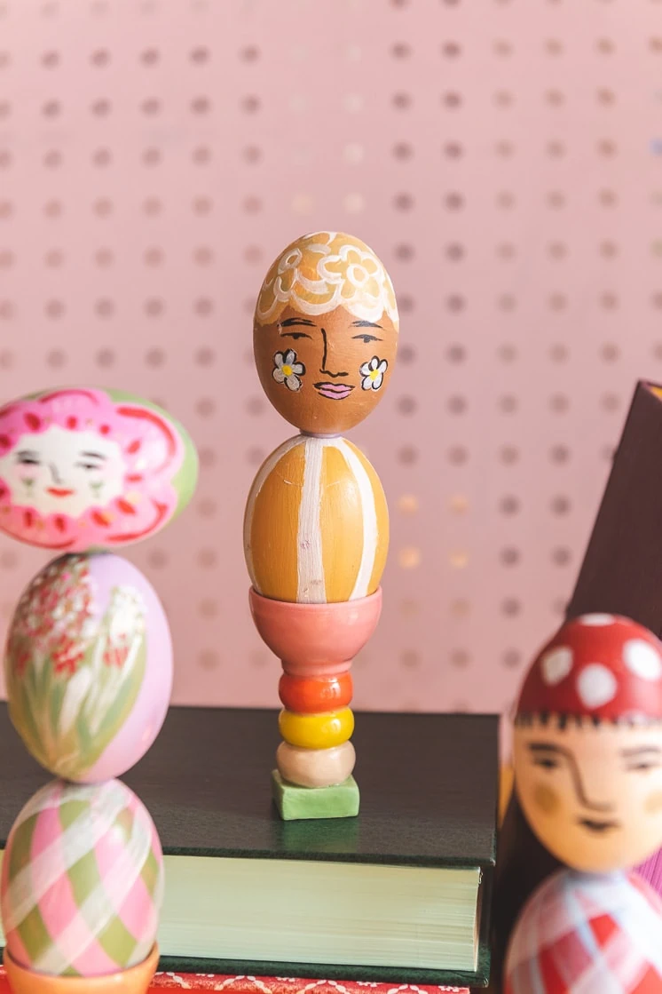 painted Easter egg columns perched on colorful books against a pink background.