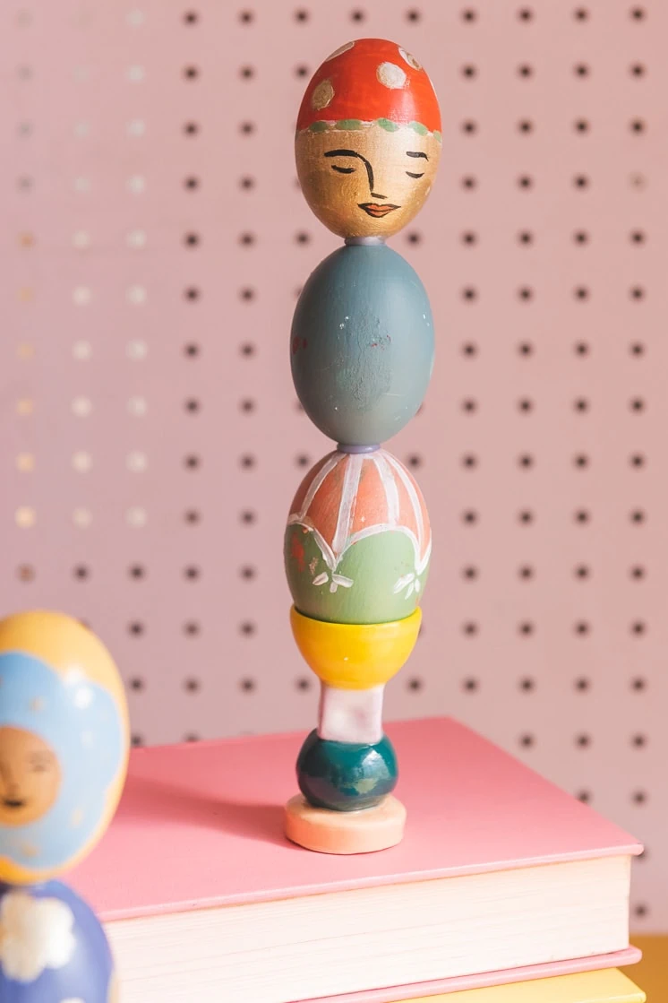Colorful painted easter egg columns stacked on books against a pink background.
