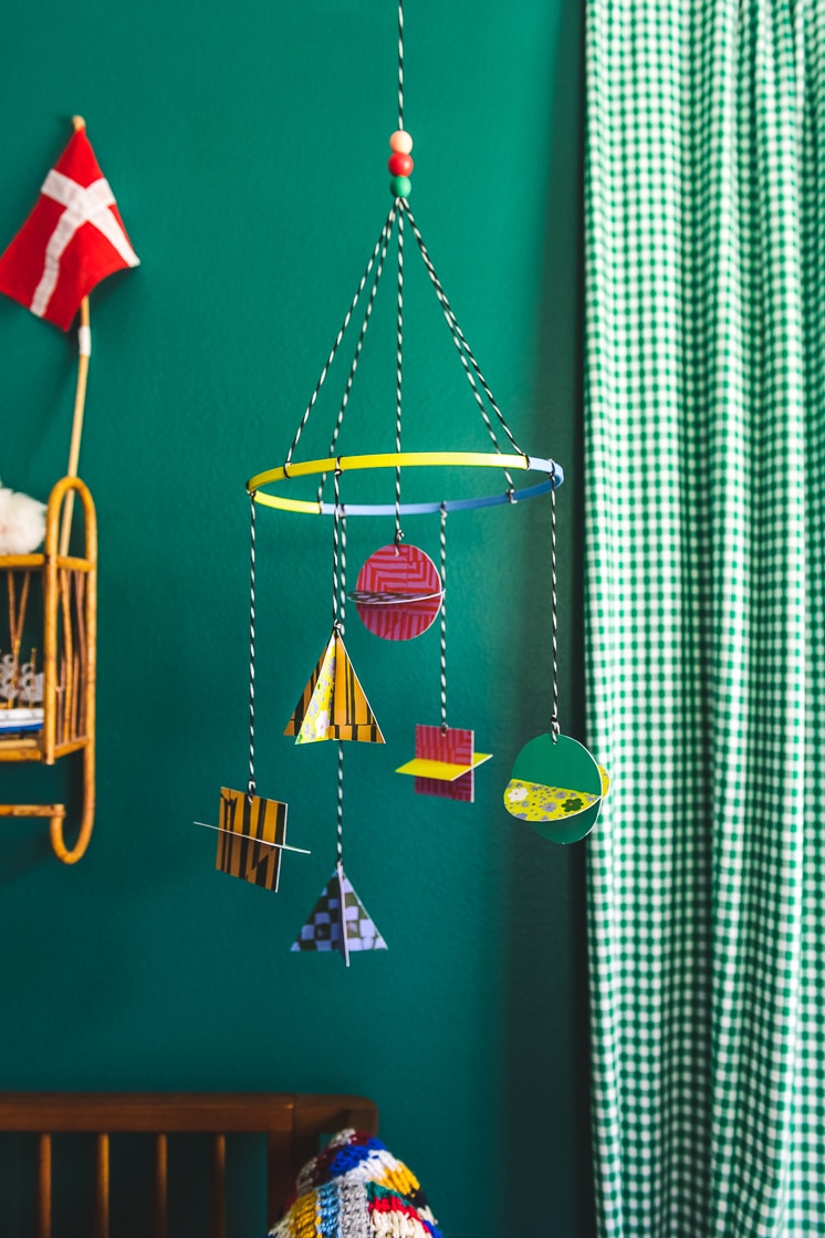Colorful, geometric paper shapes hang from a mobile in a green room.