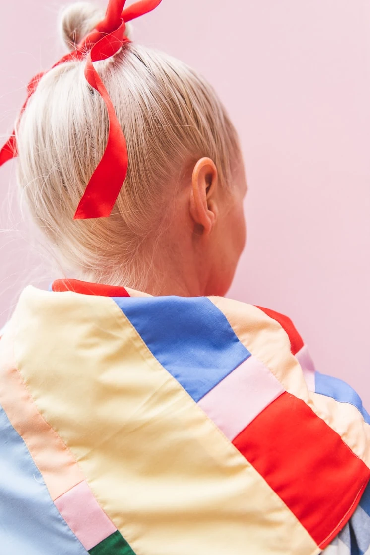 Brittany wearing a patchwork bandana over her shoulders. Her hair is tied up with a bright red ribbon and she's in front of a pink backdrop.