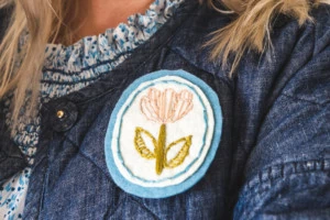 Closeup of the embroidered floral brooch on Brittany's chambray quilted coat.