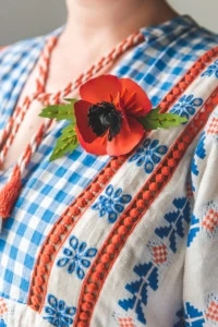 Brittany wears a paper poppy with accenting embroidery on a woven blouse.