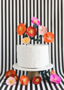 Paper poppies in bright colors as a cake topper against a striped background