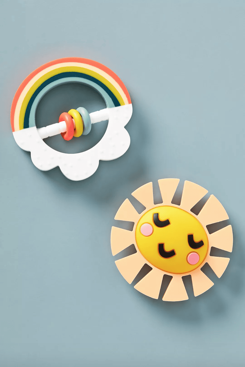 Silicone teether toys on a baby blue background. One is a smiling sun, one is a rainbow with a cloud.