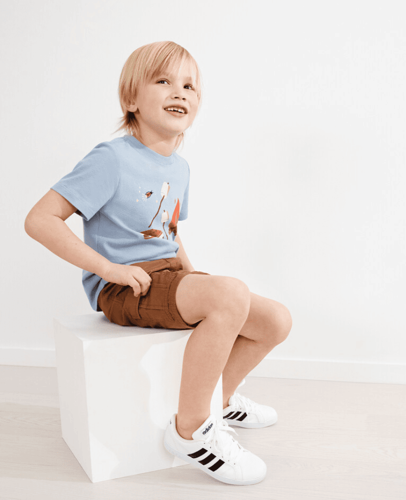 Boy wearing a blue tee and brown shorts sits on a white box and smiles