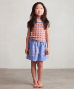 A girl wears a pink, orange, and blue jacquard tank top with a blue rick rack trimmed skirt
