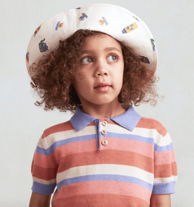 A girl wears a knitted button up shirt and a hat.
