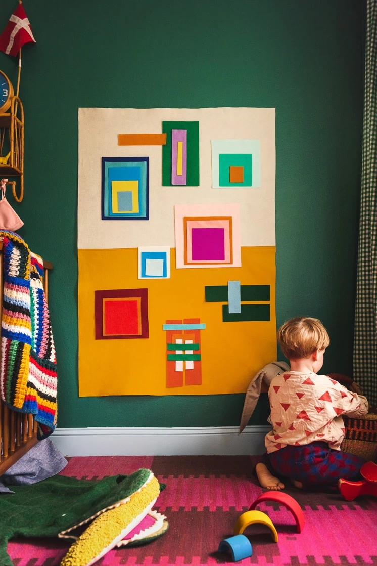 Jasper sits in front of a colorful Josef Albers-inspired felt board in a colorful room