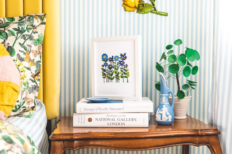 Field of Colored Flowers Papercut print by Julie Marabelle on a stack of books in a blue striped bedroom