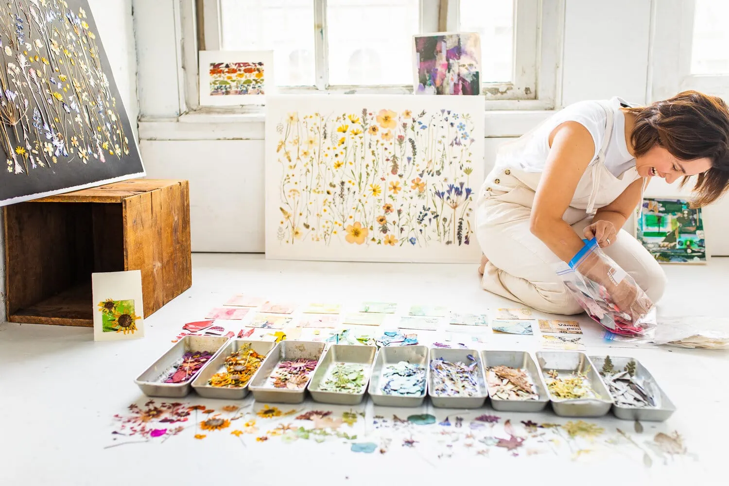 Tricia Paoluccio sits in front of pressed flowers in color coded trays in a light-filled room