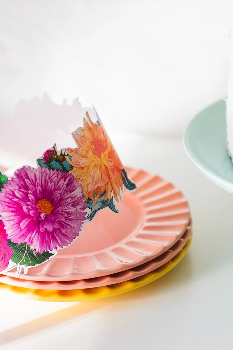 Detailed drawings of flowers make up a fuchsia and orange flower crown, which is resting on a pile of sherbet-colored plates.