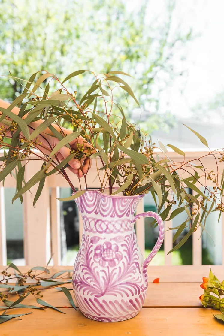 A person arranges eucalyptus branches in a purple and white vase.