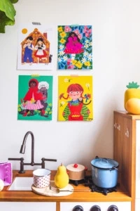 Four illustrations from fairytales hung above a child's kitchen toy set.
